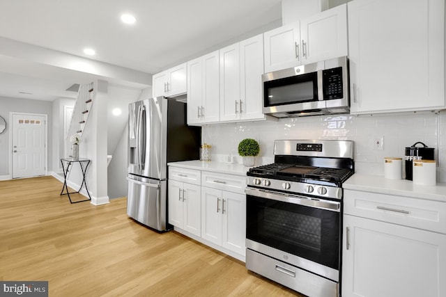 kitchen with decorative backsplash, light hardwood / wood-style floors, white cabinetry, and appliances with stainless steel finishes