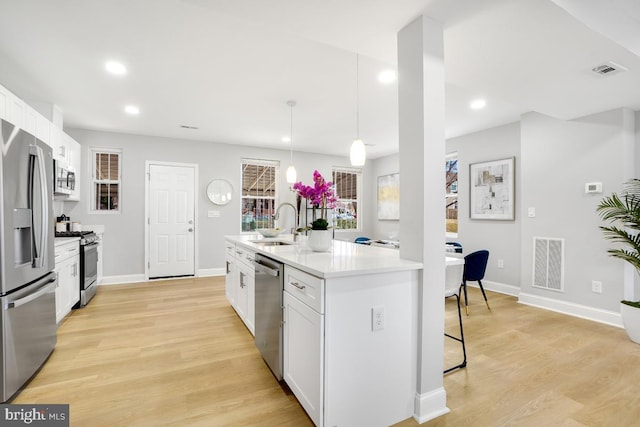 kitchen with appliances with stainless steel finishes, pendant lighting, white cabinets, light hardwood / wood-style floors, and an island with sink