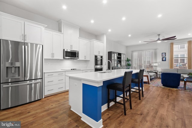 kitchen featuring a kitchen island with sink, ceiling fan, appliances with stainless steel finishes, a kitchen bar, and white cabinetry