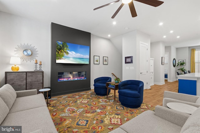 living room featuring ceiling fan, a fireplace, and light wood-type flooring