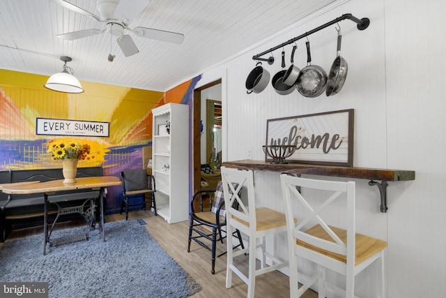 dining area featuring ornamental molding, light hardwood / wood-style floors, ceiling fan, and wooden walls