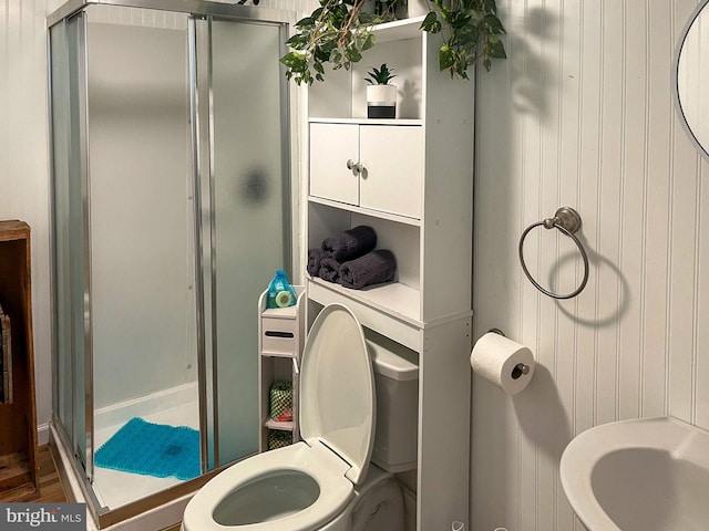 bathroom featuring toilet, a shower with door, and wooden walls