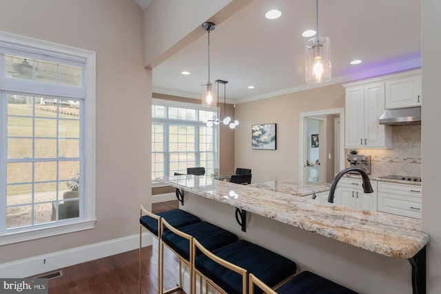 kitchen featuring decorative light fixtures, a kitchen bar, white cabinetry, and backsplash