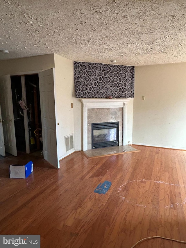 unfurnished living room featuring hardwood / wood-style flooring, a textured ceiling, and a high end fireplace