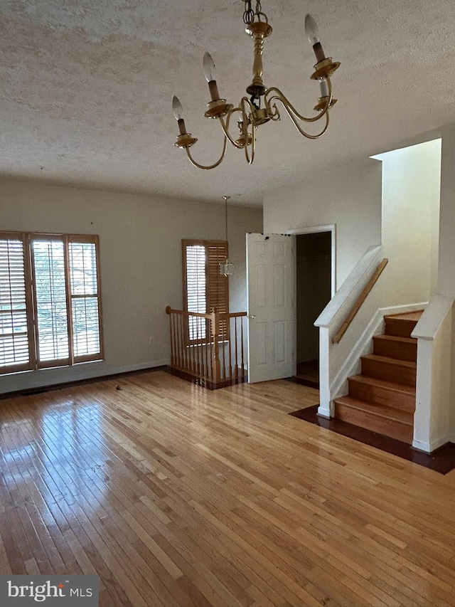 unfurnished living room with hardwood / wood-style floors, a textured ceiling, and an inviting chandelier