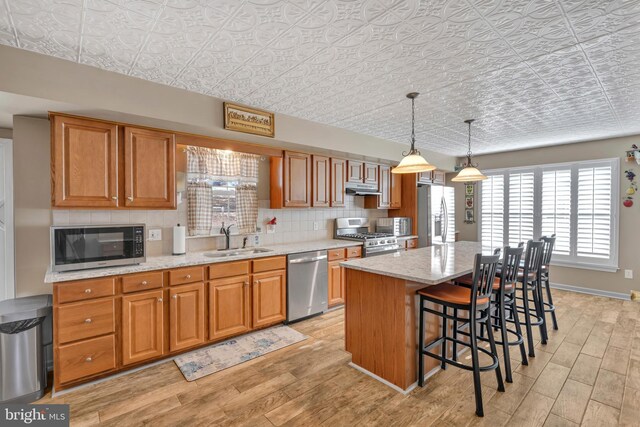 kitchen featuring a kitchen bar, light stone countertops, stainless steel appliances, sink, and a kitchen island