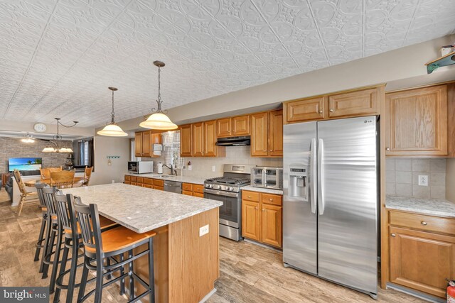 kitchen featuring sink, decorative backsplash, appliances with stainless steel finishes, a kitchen island, and a kitchen bar