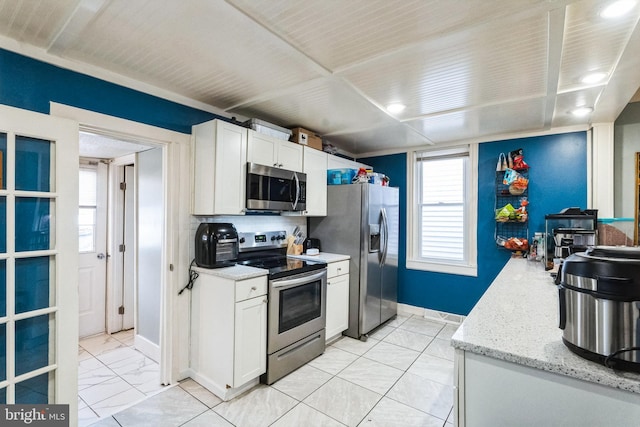 kitchen with white cabinets, stainless steel appliances, light stone countertops, and a healthy amount of sunlight