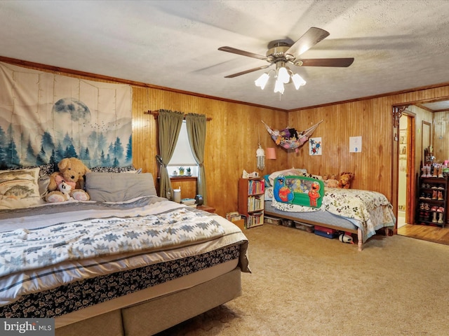 carpeted bedroom with a textured ceiling, ceiling fan, ornamental molding, and wood walls