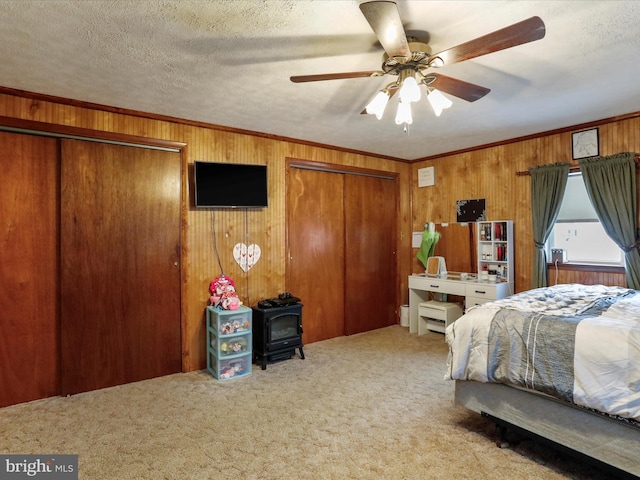 carpeted bedroom featuring a textured ceiling, a wood stove, ceiling fan, and wooden walls