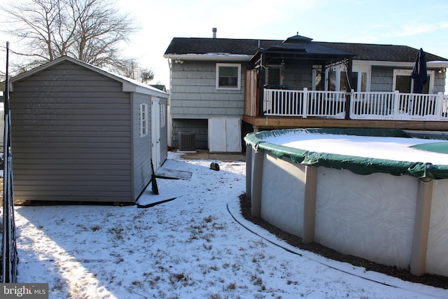 snow covered rear of property with a covered pool and cooling unit