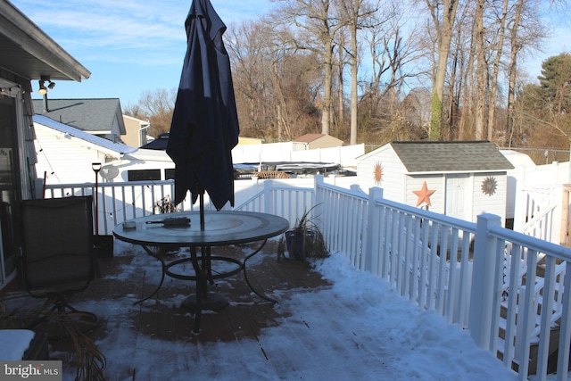 snow covered patio featuring a deck and a storage unit