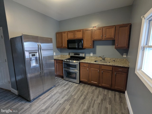 kitchen with light stone counters, appliances with stainless steel finishes, sink, and hardwood / wood-style floors