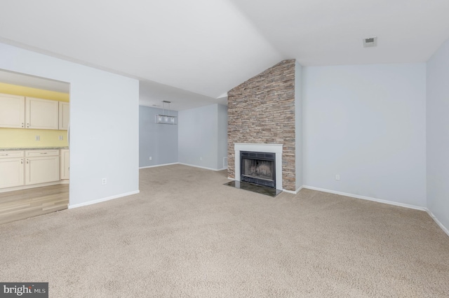 unfurnished living room with vaulted ceiling, light carpet, and a stone fireplace