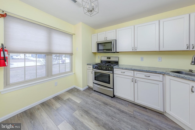 kitchen with stainless steel appliances, white cabinets, sink, and light hardwood / wood-style flooring