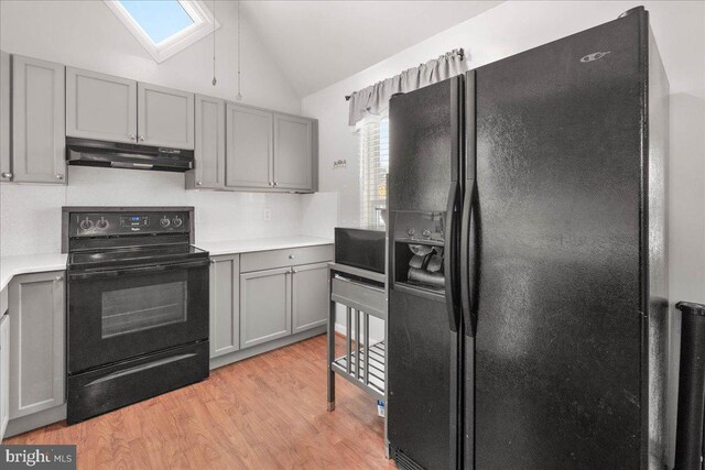 kitchen featuring black appliances, gray cabinetry, lofted ceiling with skylight, and light wood-type flooring