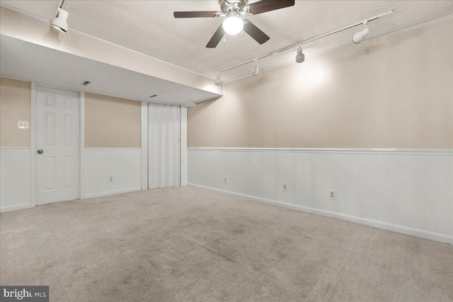 basement with a textured ceiling, track lighting, ceiling fan, and carpet floors