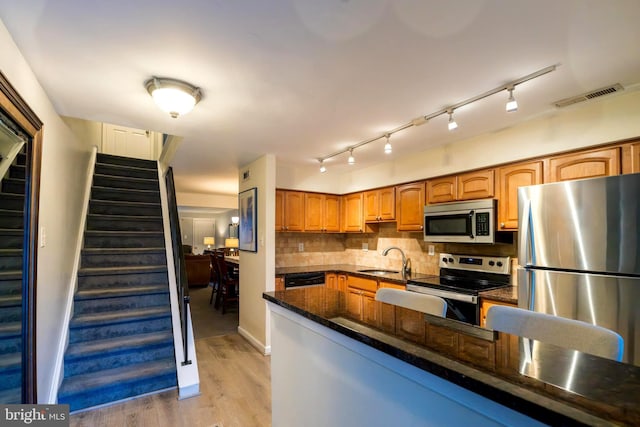 kitchen featuring decorative backsplash, light wood-type flooring, stainless steel appliances, sink, and dark stone countertops