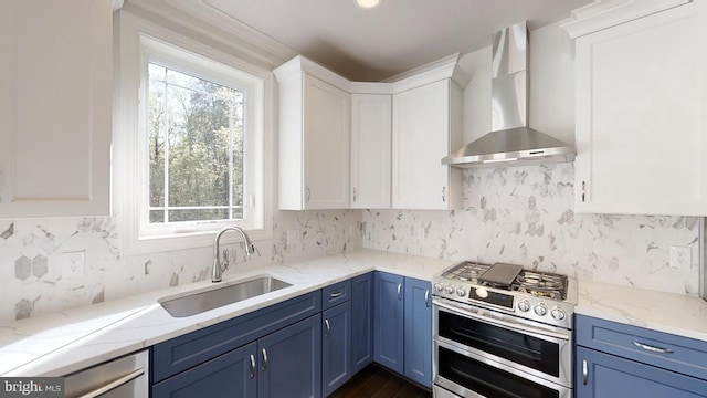 kitchen featuring stainless steel appliances, blue cabinets, sink, wall chimney range hood, and white cabinets