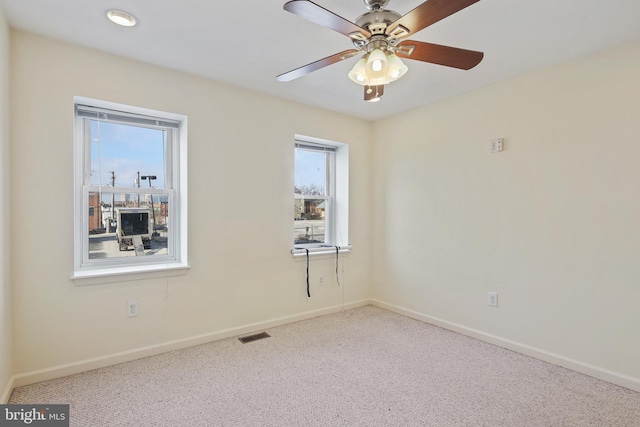 carpeted spare room with visible vents, baseboards, and a ceiling fan