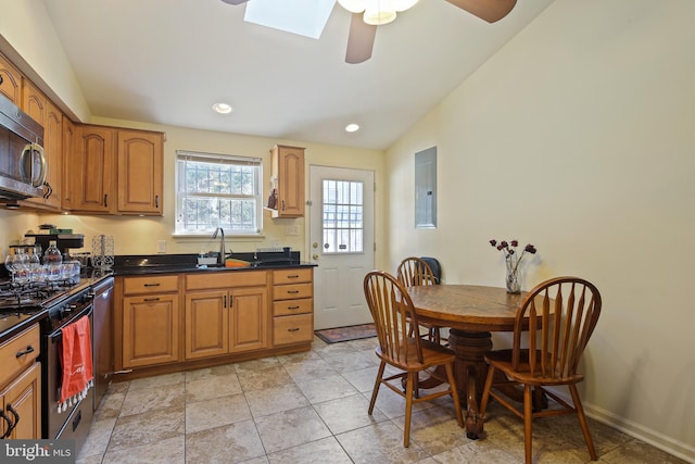 kitchen with lofted ceiling with skylight, a sink, dark countertops, appliances with stainless steel finishes, and baseboards