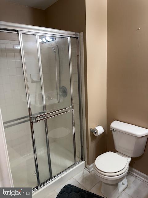 bathroom with tile patterned flooring, toilet, and a shower with shower door