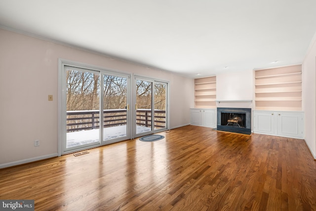 unfurnished living room featuring built in shelves, crown molding, and hardwood / wood-style flooring