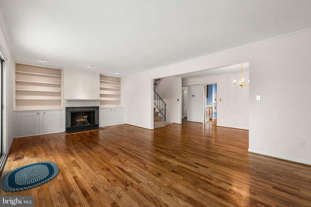 unfurnished living room featuring built in shelves, dark hardwood / wood-style flooring, and an inviting chandelier