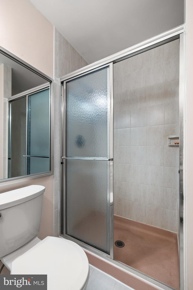 bathroom with tile patterned floors, toilet, and a shower with door