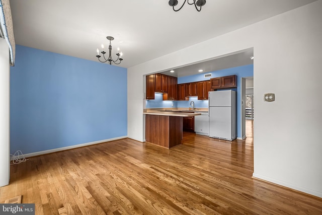 kitchen featuring pendant lighting, an inviting chandelier, white refrigerator, sink, and light hardwood / wood-style flooring