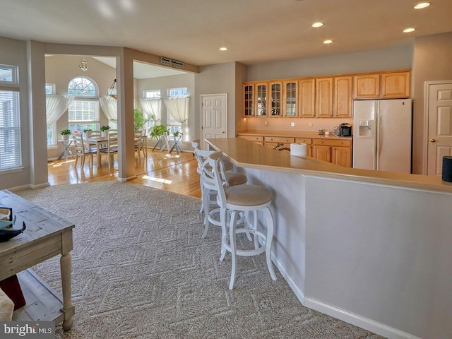 kitchen featuring light colored carpet, light brown cabinetry, and white fridge with ice dispenser