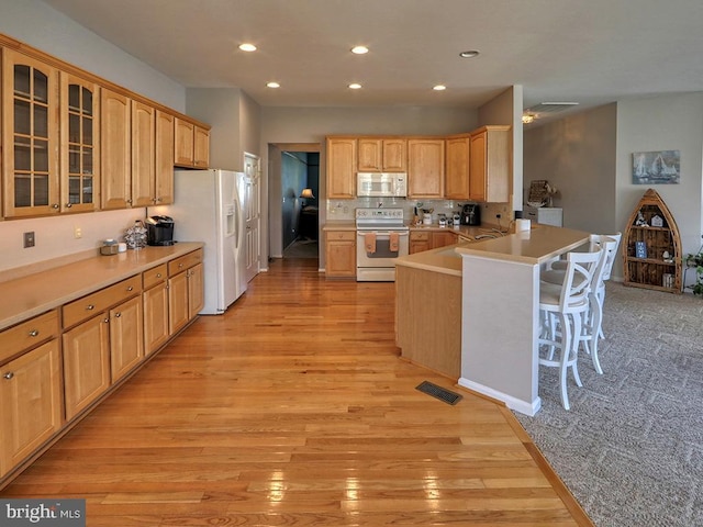 kitchen featuring white appliances, a breakfast bar area, sink, light hardwood / wood-style flooring, and tasteful backsplash