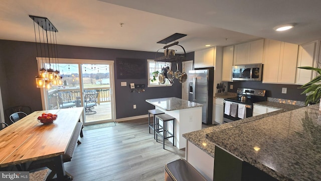 kitchen featuring stone counters, white cabinets, hanging light fixtures, appliances with stainless steel finishes, and a kitchen island