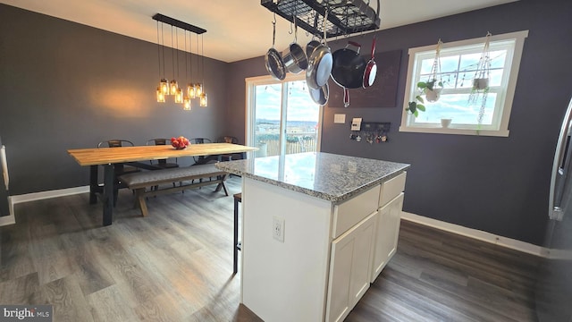 kitchen with light stone counters, decorative light fixtures, white cabinets, a center island, and dark hardwood / wood-style floors