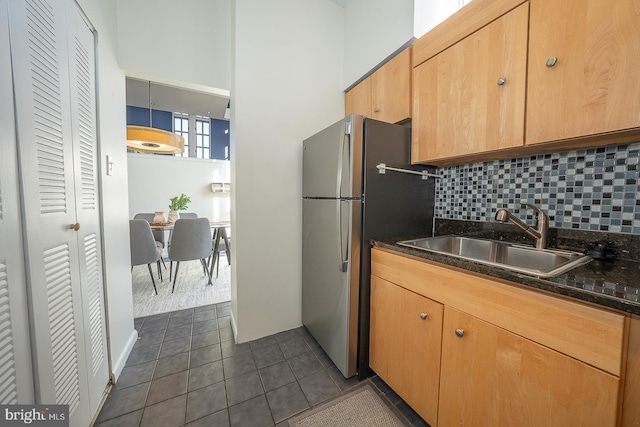 kitchen with stainless steel refrigerator, sink, dark stone counters, decorative backsplash, and dark tile patterned flooring