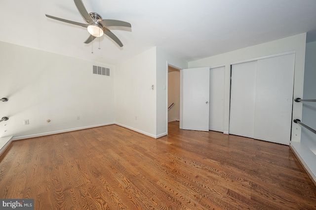 unfurnished bedroom featuring ceiling fan, wood-type flooring, and multiple closets