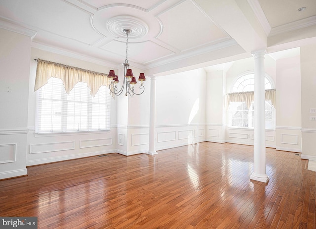 unfurnished dining area featuring wood-type flooring, an inviting chandelier, ornamental molding, and ornate columns