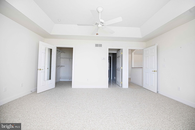 unfurnished bedroom with light carpet, a tray ceiling, a spacious closet, and ceiling fan