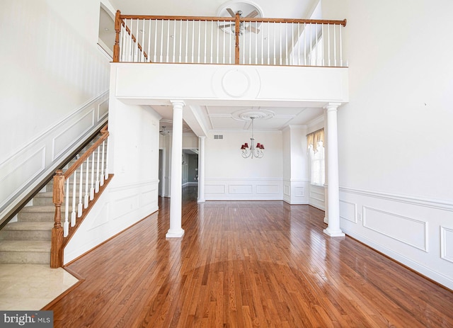 unfurnished living room featuring a chandelier, hardwood / wood-style flooring, and ornate columns