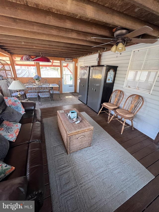 living room featuring ceiling fan, wood walls, beamed ceiling, and dark hardwood / wood-style floors