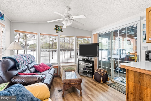 living room with ceiling fan, lofted ceiling, a textured ceiling, and light hardwood / wood-style flooring