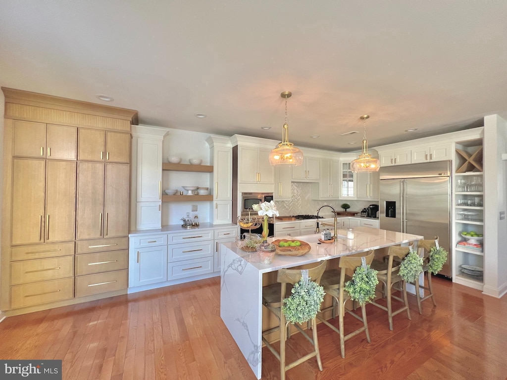 kitchen featuring pendant lighting, a large island with sink, built in appliances, a kitchen bar, and white cabinetry