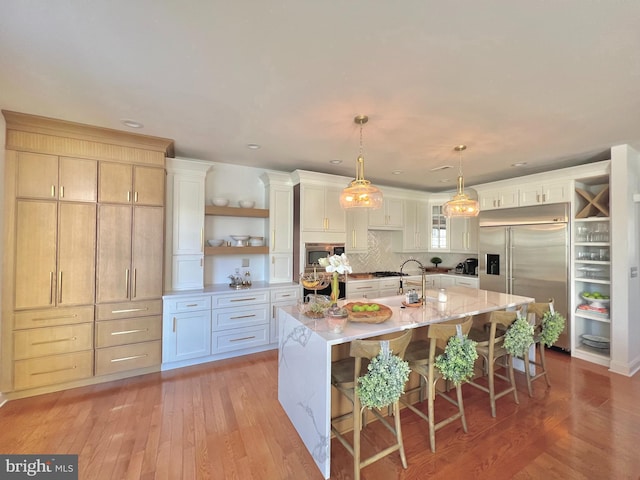 kitchen featuring pendant lighting, a large island with sink, built in appliances, a kitchen bar, and white cabinetry