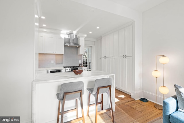 kitchen with white cabinetry, wall chimney exhaust hood, pendant lighting, light hardwood / wood-style floors, and decorative backsplash