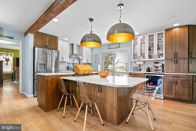 kitchen with backsplash, a kitchen island, a kitchen bar, wall chimney exhaust hood, and beverage cooler