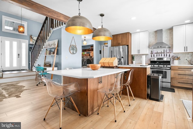 kitchen with appliances with stainless steel finishes, decorative backsplash, hanging light fixtures, wall chimney range hood, and white cabinets