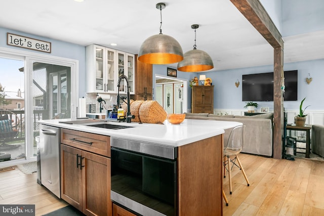 kitchen with pendant lighting, stainless steel dishwasher, light hardwood / wood-style flooring, and a kitchen island with sink