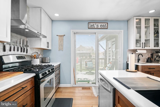 kitchen featuring white cabinets, decorative backsplash, wall chimney exhaust hood, and stainless steel appliances