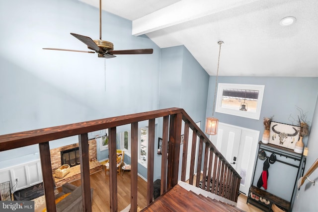 stairs featuring ceiling fan, vaulted ceiling with beams, a stone fireplace, and hardwood / wood-style floors