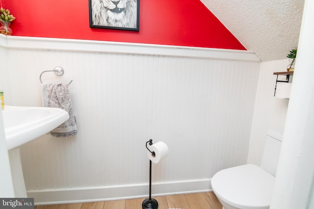 bathroom featuring toilet, vaulted ceiling, wood-type flooring, sink, and a textured ceiling